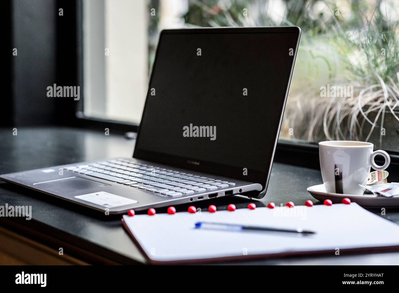 Laptop, Notebook und Espresso an einem modernen Arbeitsplatz am Fenster, ideal für Fernarbeit, Studium oder kreative Projekte. Stockfoto