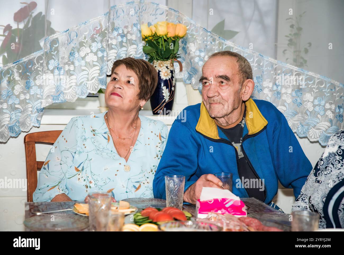 Ein russisches Paar, beide über 70 Jahre alt, schaut auf einen Fernseher. Sie sind festlich gekleidet, mit Brillen auf dem Feiertagstisch in t Stockfoto