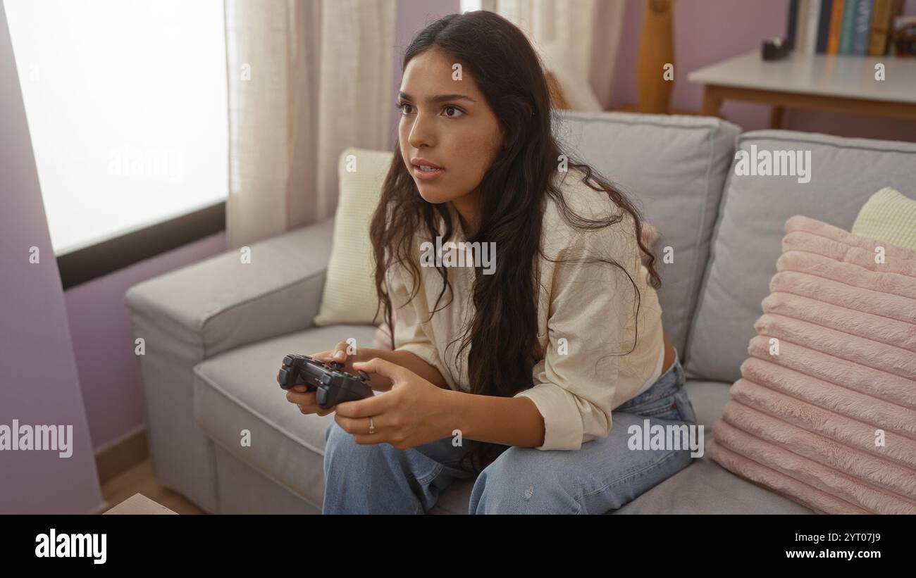 Junge Frau, die Videospiele in einem Wohnzimmer spielt und eine entspannte Atmosphäre mit lässiger Kleidung und fokussiertem Ausdruck bietet. Stockfoto