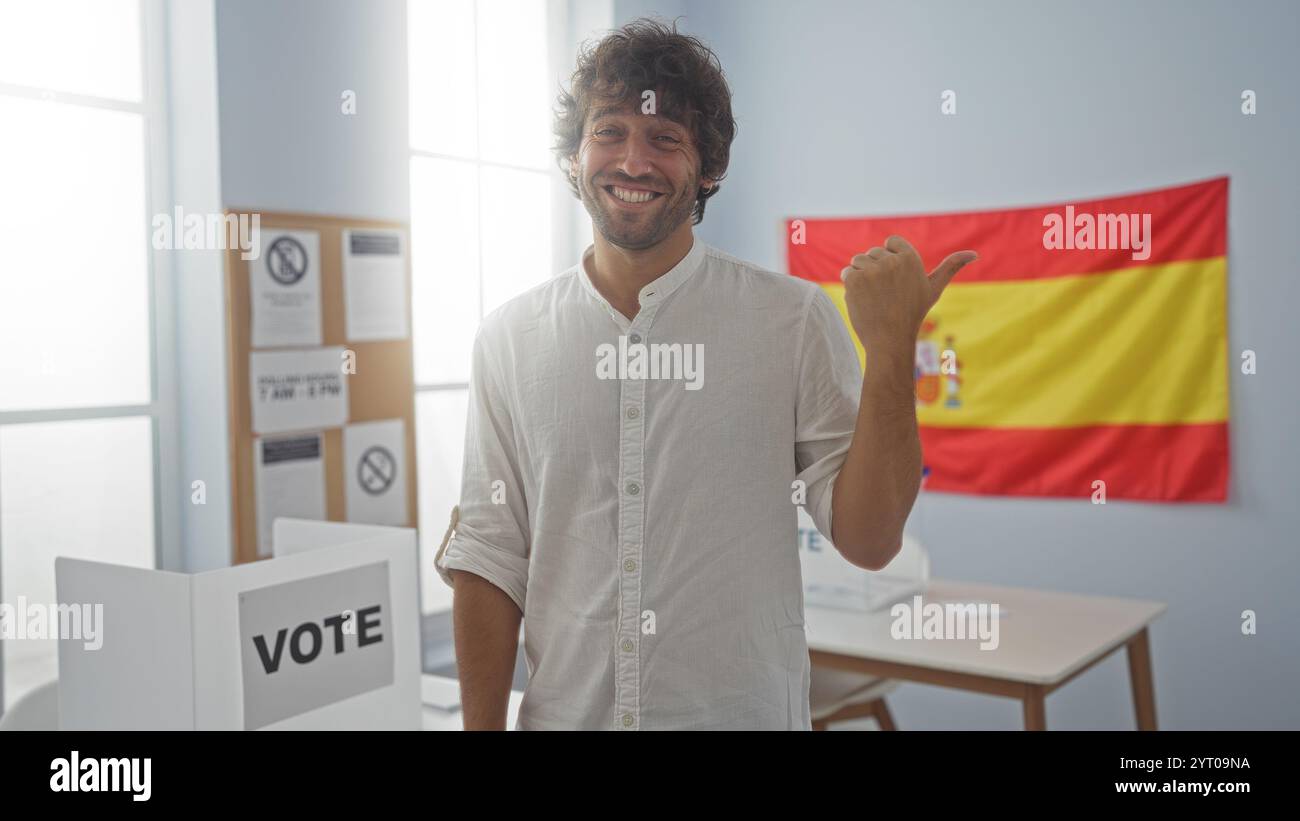 Ein lächelnder junger Mann, der auf die spanische Flagge in der Halle der Wahlschule zeigt Stockfoto