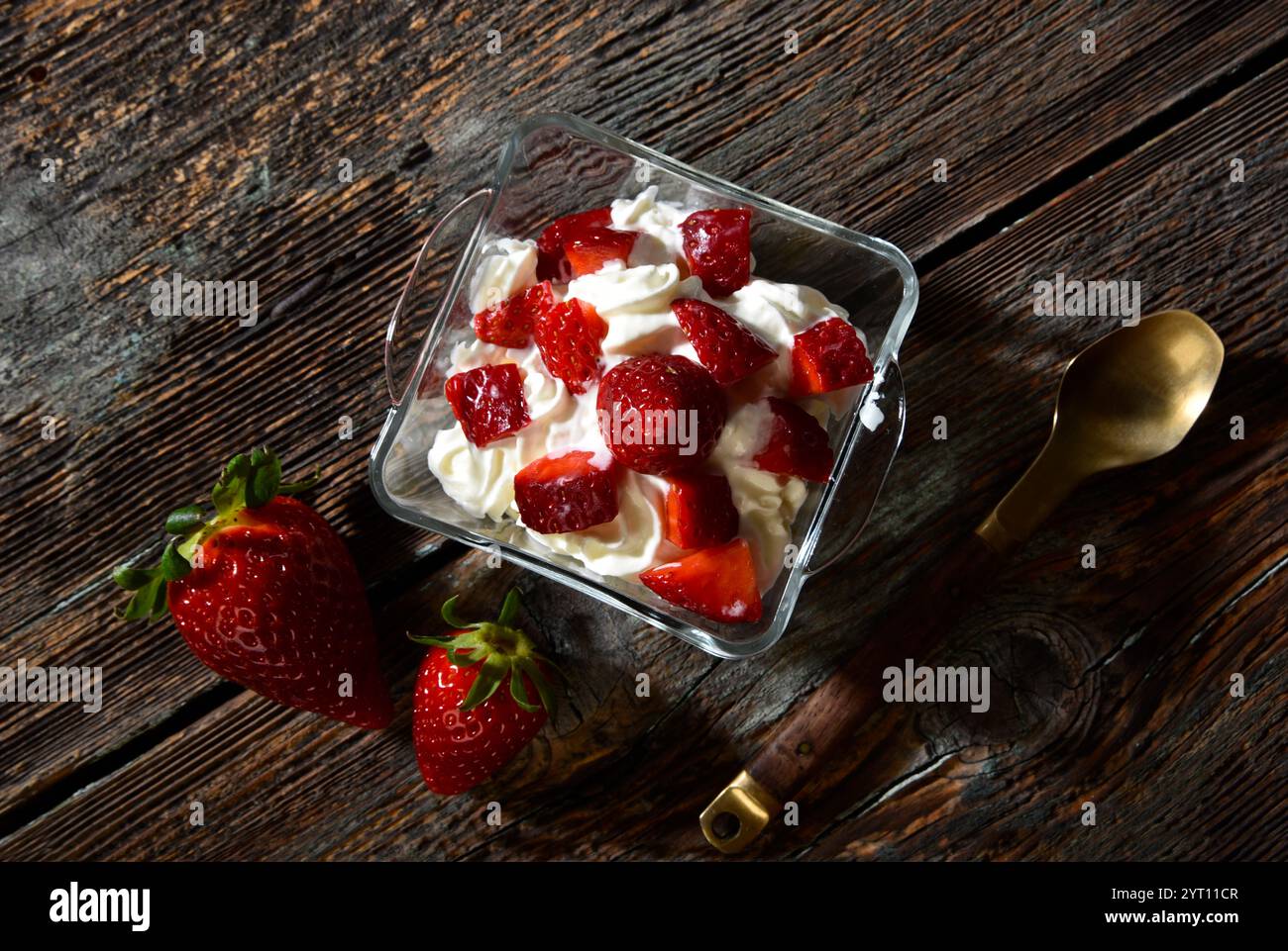 Köstliche Erdbeeren mit Schlagsahne serviert in einer weißen Untertasse auf einem rustikalen Holztisch Stockfoto