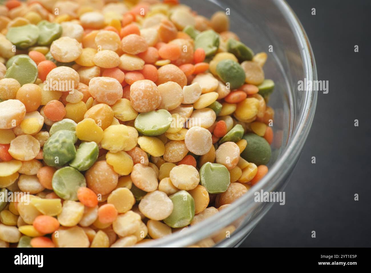 Verschiedene bunte Spaltleguminosen in einer Glasschale auf schwarzem Hintergrund. (Erbsen, Linsen). Nahaufnahme. Stockfoto