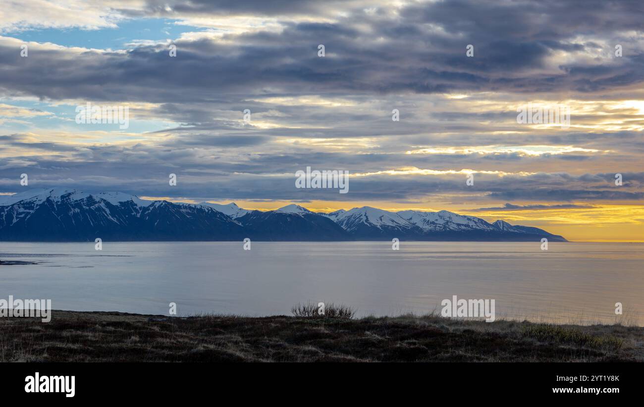 Skjalfandi (Skjalfandafloi) Fjord in Nordisland, Blick auf den orangefarbenen Sonnenuntergang mit schneebedeckten Viknafjoll- und Kinnarfjoll-Gebirgszügen, dramatischer Himmel. Stockfoto