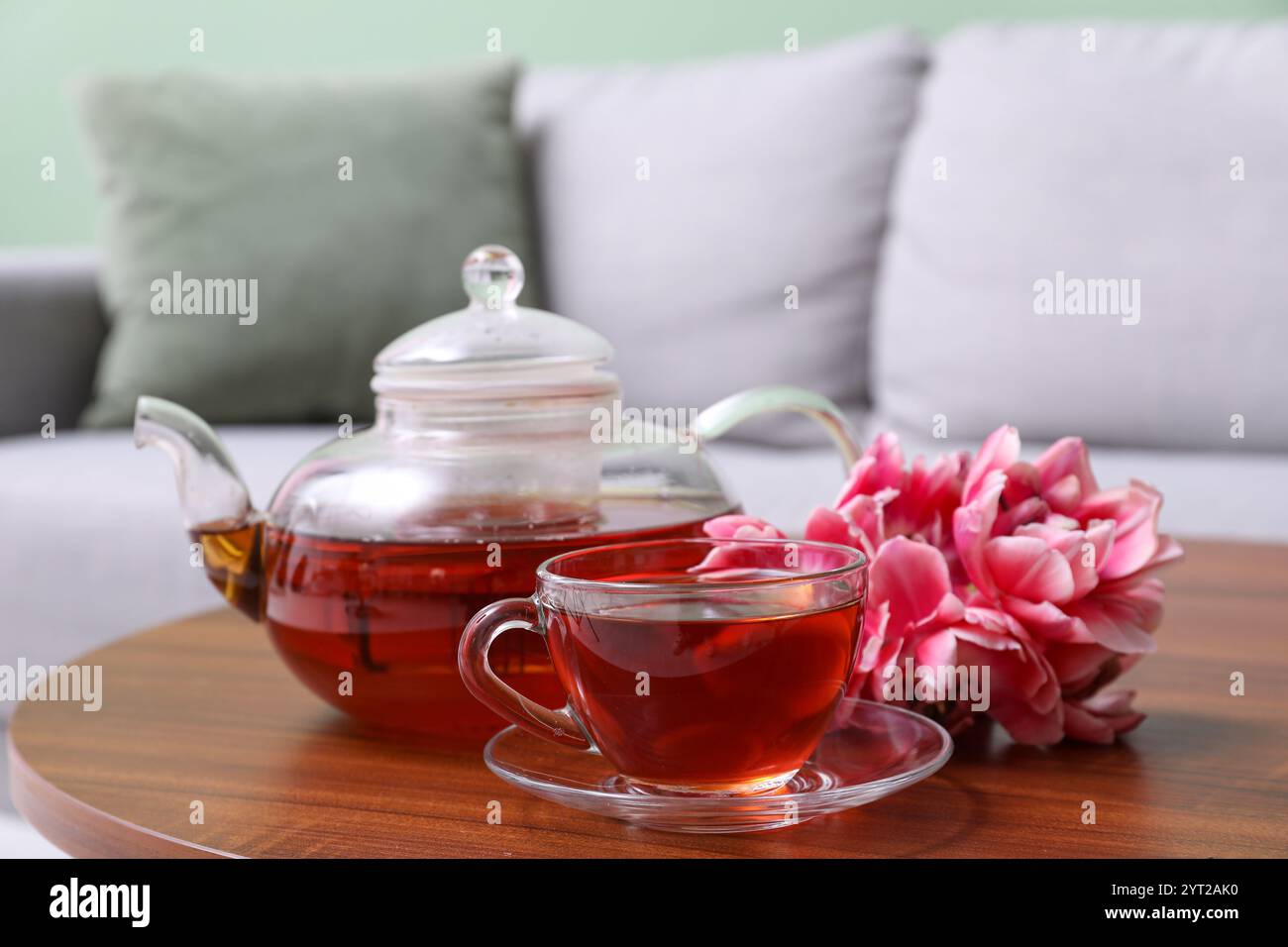 Transparente Tasse Tee und Teekanne auf dem Tisch mit Tulpenblüten im Wohnzimmer Stockfoto