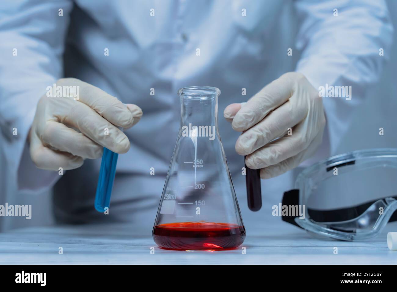 Ein Wissenschaftler hält ein mit grüner Flüssigkeit gefülltes Reagenzglas in einem Labor, umgeben von verschiedenen Laborgeräten. Das Bild hebt den Fokus und die Precis hervor Stockfoto