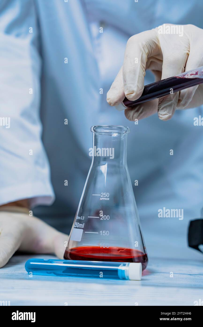 Ein Wissenschaftler hält ein mit grüner Flüssigkeit gefülltes Reagenzglas in einem Labor, umgeben von verschiedenen Laborgeräten. Das Bild hebt den Fokus und die Precis hervor Stockfoto