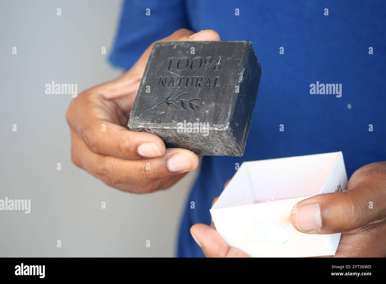 Halten Sie mit der Hand vorsichtig einen Streifen schwarzer Seife in einer offenen Box Stockfoto