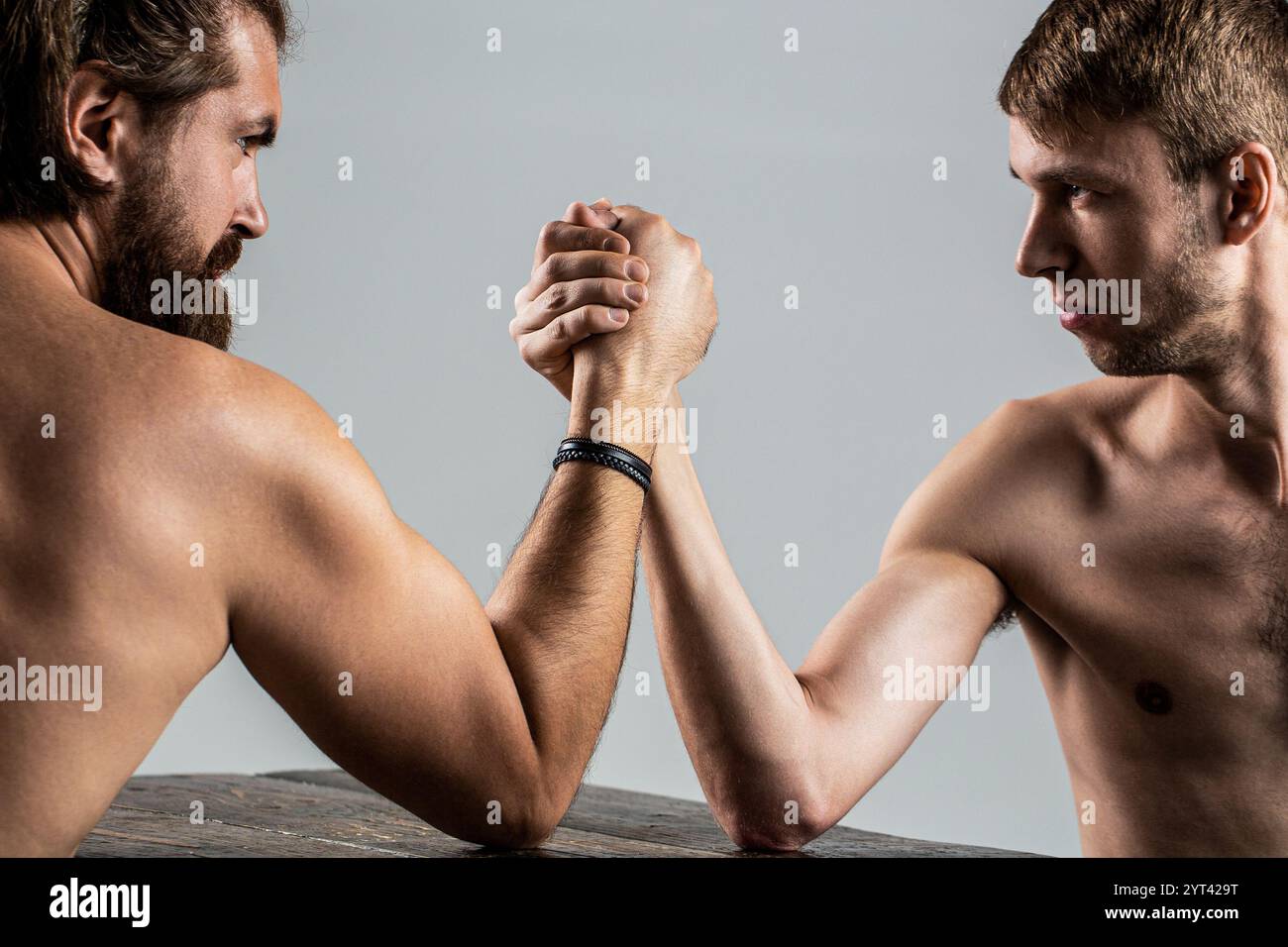 Armringen. Zwei Mannshände schlossen den Arm, stark und schwach, ungleich. Schwer bemuskelter bärtiger Mann Arm, der einen schwachen Mann ringt Stockfoto