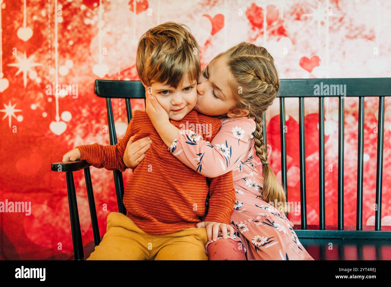 Schwester küsst brotherâ Wange auf schwarzer Bank, Herzhintergrund Stockfoto