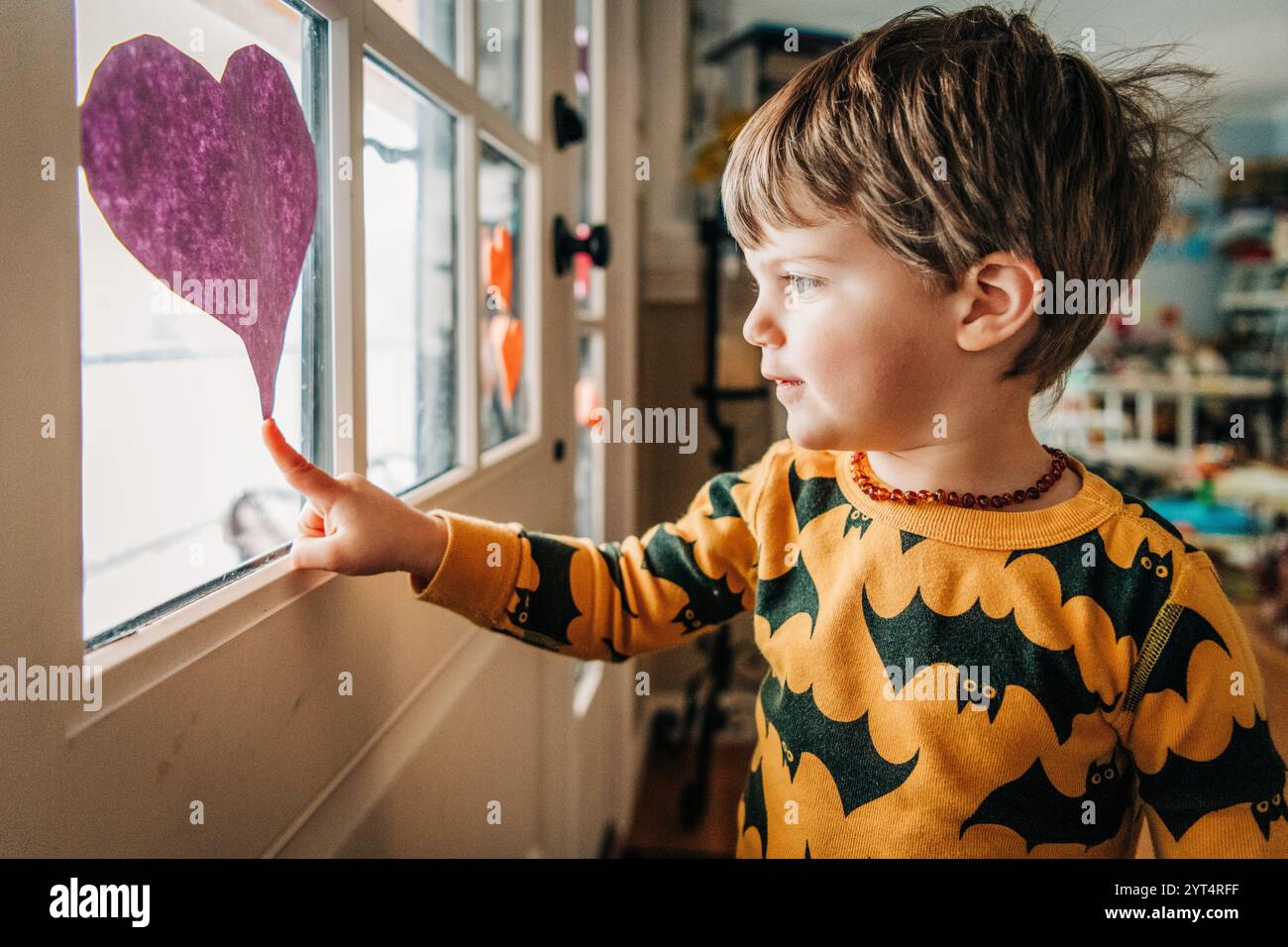 Kleinkinder im Schlafanzug mit Fledermausmuster zeigen auf ein lila Herz am Fenster Stockfoto