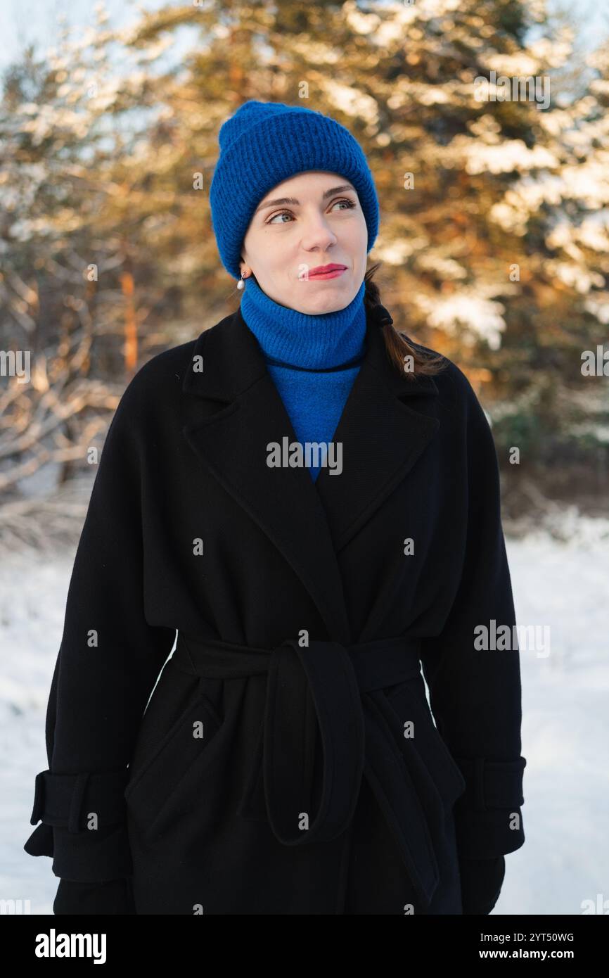 Junge Erwachsene Frau, die im Winterwald wegschaut Stockfoto