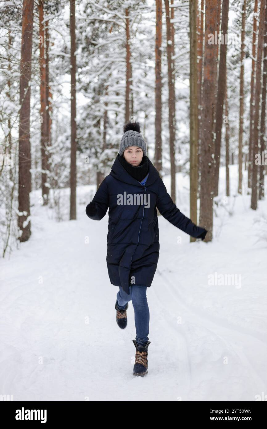 Frau, die durch den verschneiten Kiefernwald läuft Stockfoto
