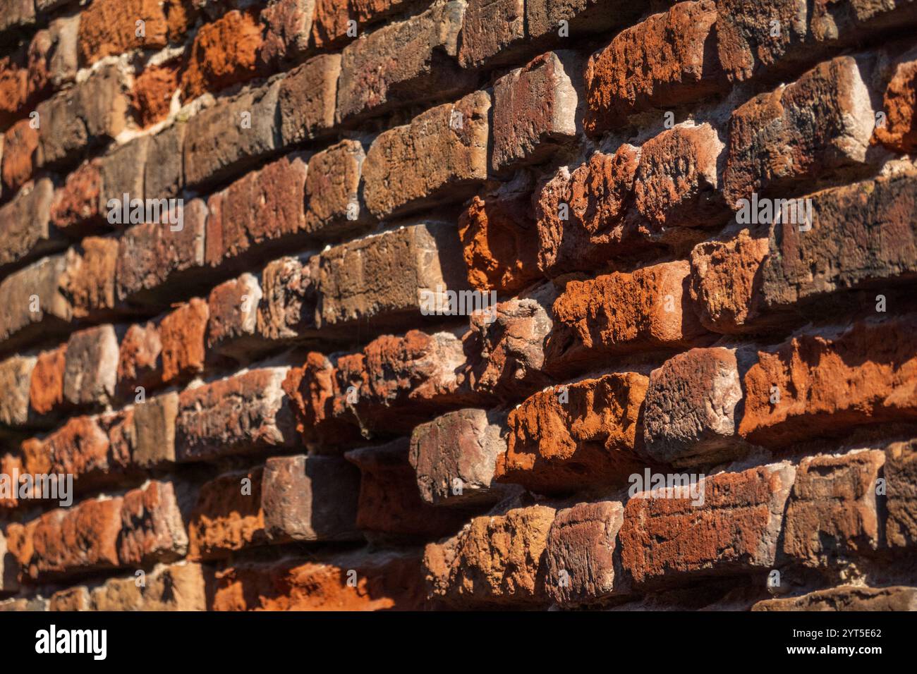 Detaillierte Ansicht der rustikalen Ziegelwand mit Texturen und Farben unter Sonnenlicht. Ideal für Hintergründe oder architektonische Themen. Stockfoto