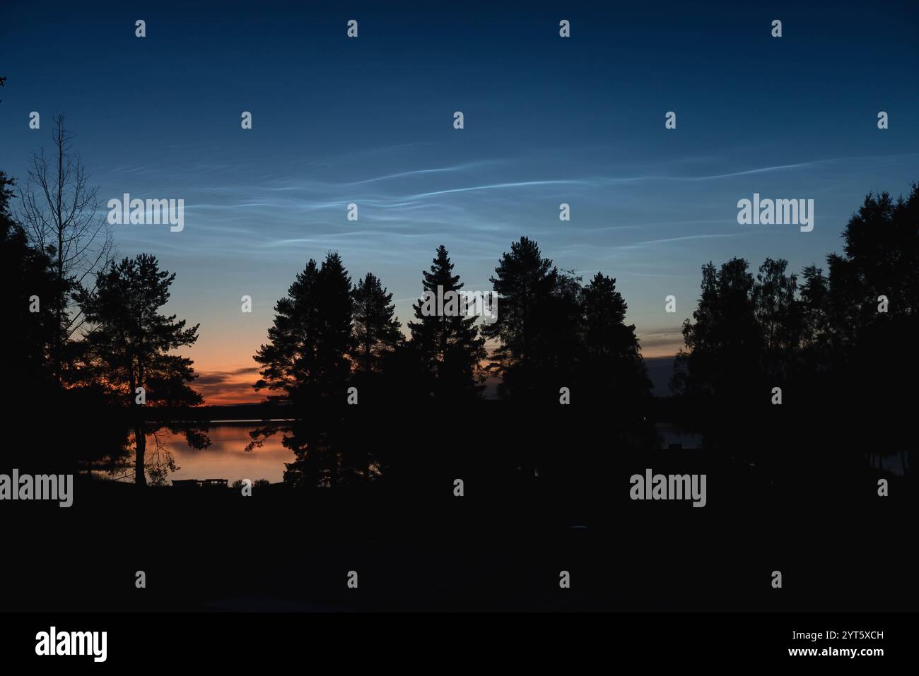 Während der Sommersonnenwende reflektieren wunderschöne, nachtschwärzende Wolken auf dem ruhigen Wasser eines Sees und schaffen mit dem Silhouett eine magische Atmosphäre Stockfoto