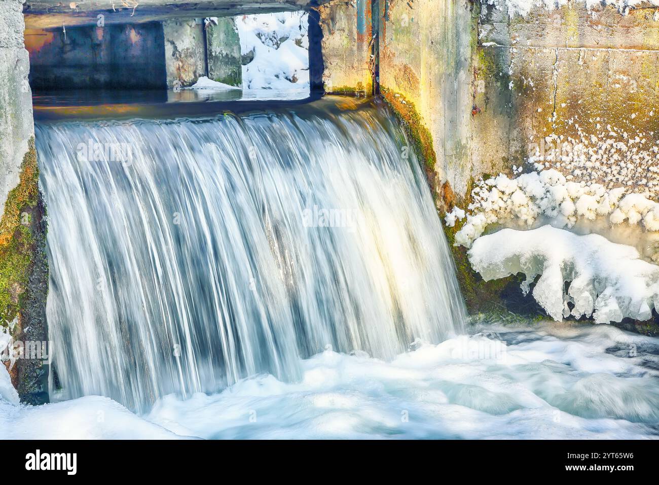 Landschaftsfoto eines nicht gefrorenen Flusses mit schneller Strömung und Stromschnellen an düsteren kalten Wintertagen. Kleiner Wasserfall mit Bewegungsunschärfe Stockfoto