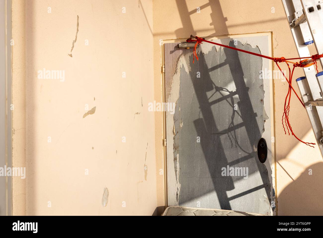 Der kantige Schatten einer zusammenklappbaren Stahlleiter erstreckt sich über eine gelbe Wand und erzeugt scharfe Kontraste und geometrische Muster. Stockfoto