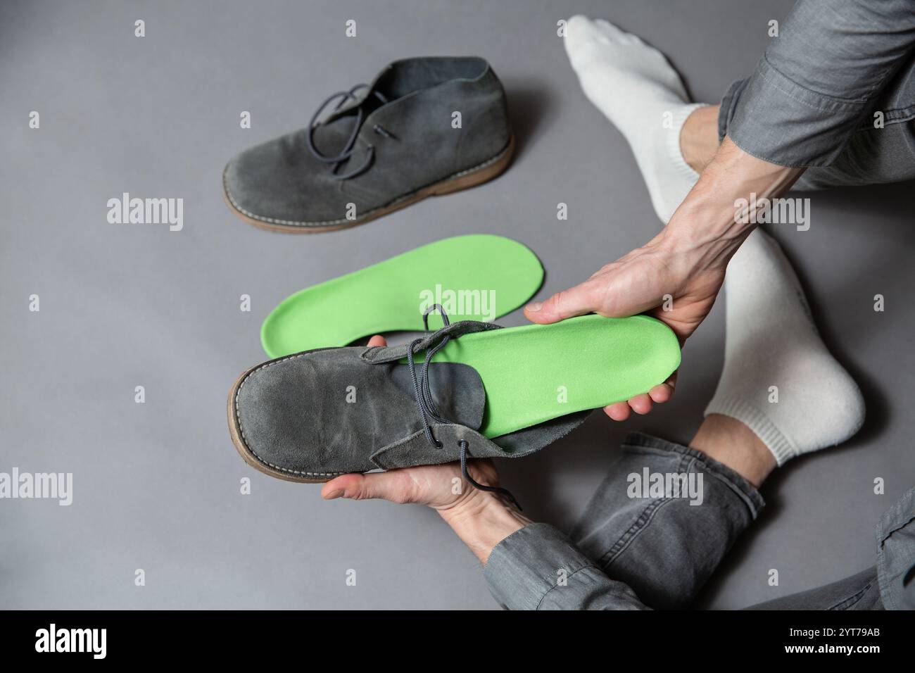 Nahaufnahme von Männerhänden, die grüne orthopädische Einlegesohlen in graue Schuhe stecken. Medizinische und orthopädische Behandlung und Prävention von Plattfüßen Co Stockfoto