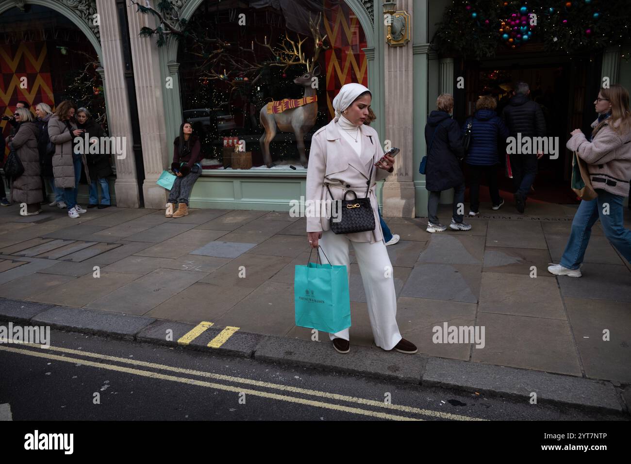 Frau, die ein Hijab-Kopftuch trug und ihr Smartphone surfte, während sie vor Fortnum & Mason stand, Piccadilly, London, England, Vereinigtes Königreich Stockfoto Frau, die ein Hijab-Kopftuch trug und ihr Smartphone surfte, während sie vor Fortnum & Mason stand, Piccadilly, London, England, Vereinigtes Königreich Stockfoto