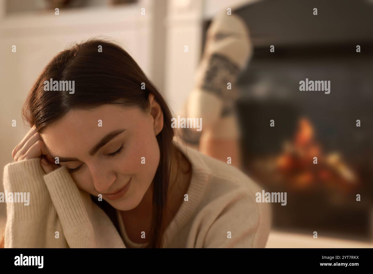 Frau in warmem Pullover, die zu Hause neben dem Kamin ruht Stockfoto