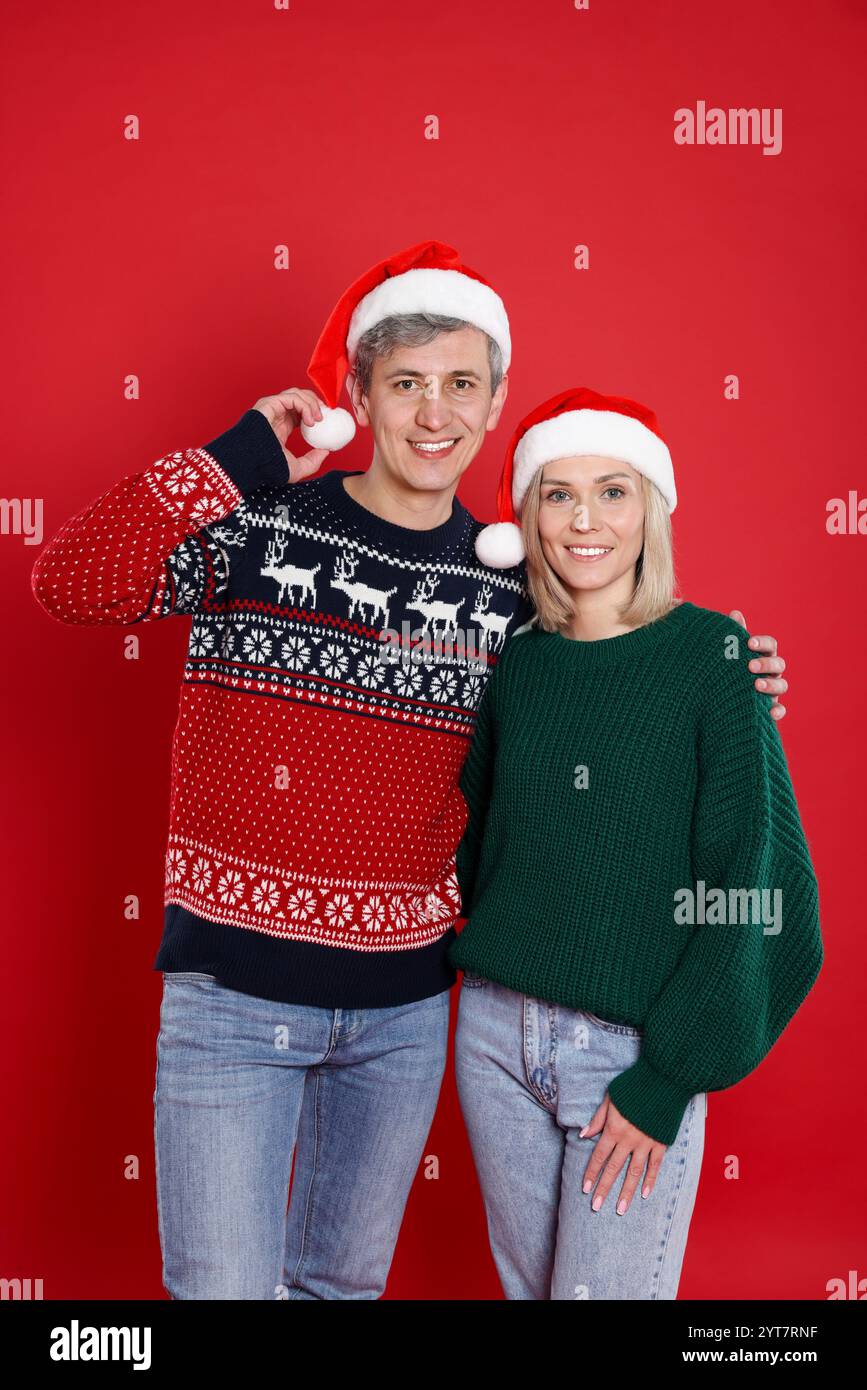 Glückliches Paar in Weihnachtsmützen auf rotem Hintergrund. Weihnachtsfeier Stockfoto