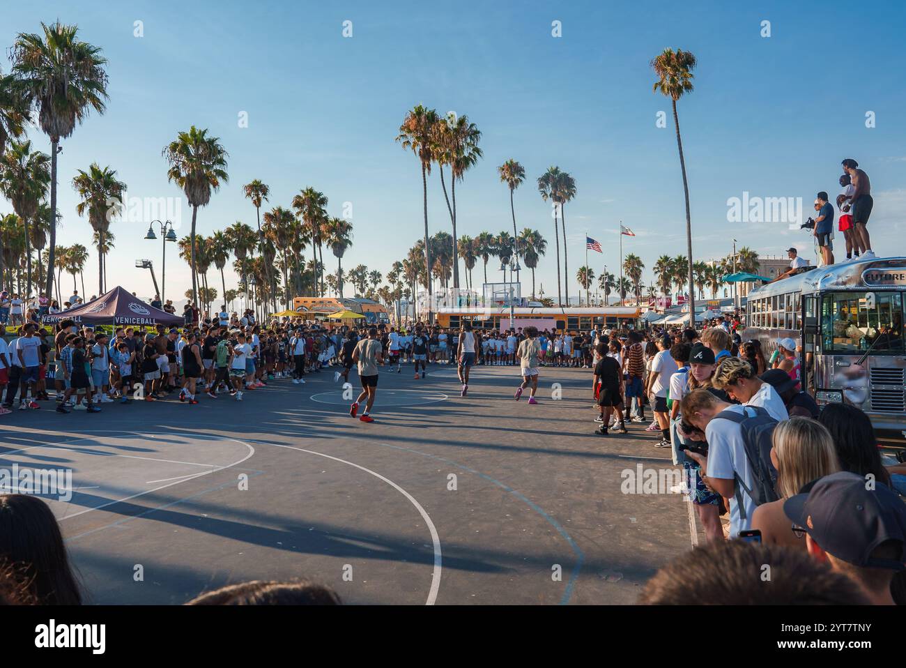 Eine lebhafte Szene am Venice Beach, Los Angeles, bietet ein Basketballspiel, umgeben von einer lebhaften Menschenmenge, Palmen und Food Trucks darunter Stockfoto