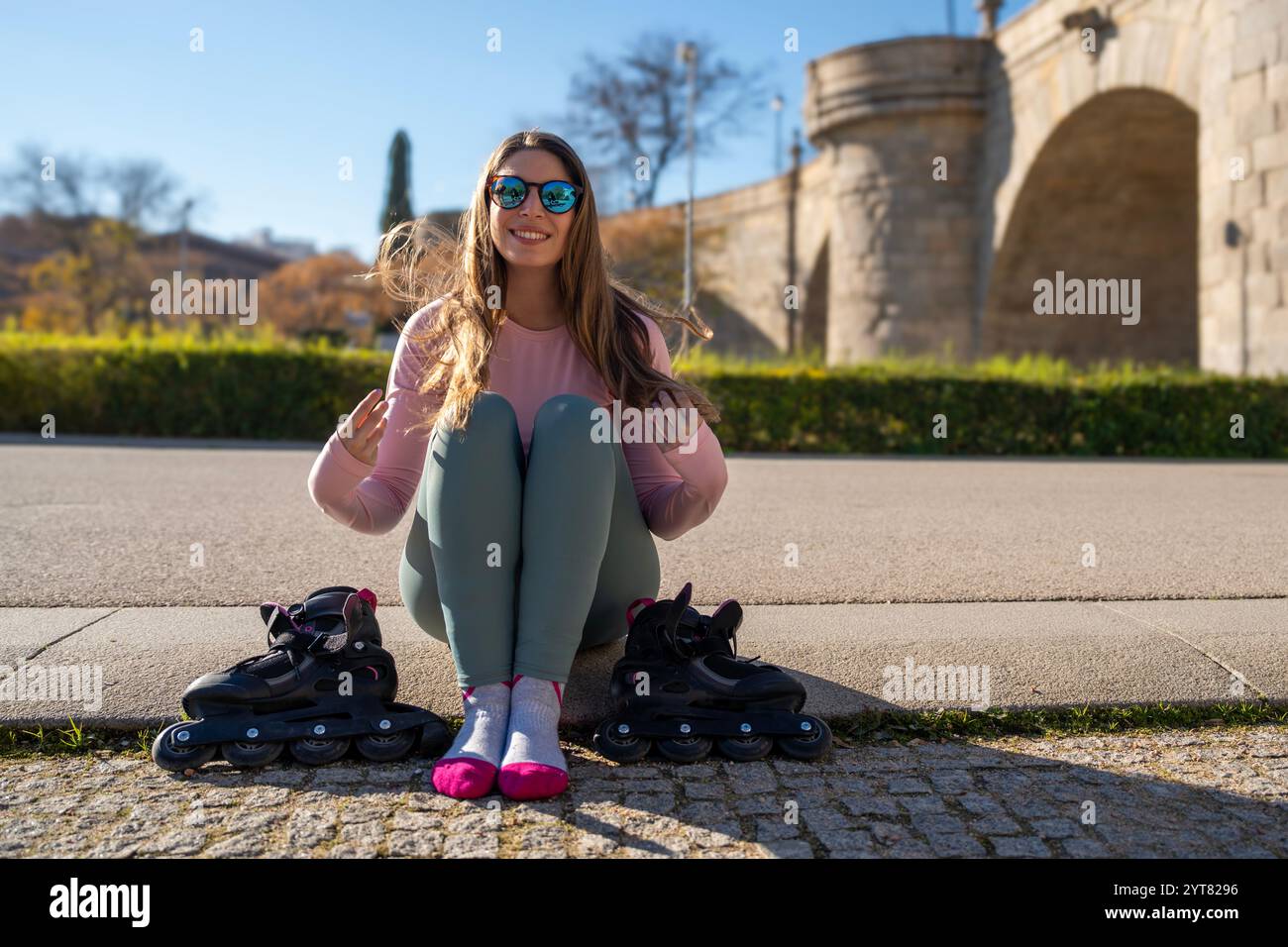 Sportliche Frau, die sich nach Inlineskaten im Park nahe der Brücke ausruht Stockfoto