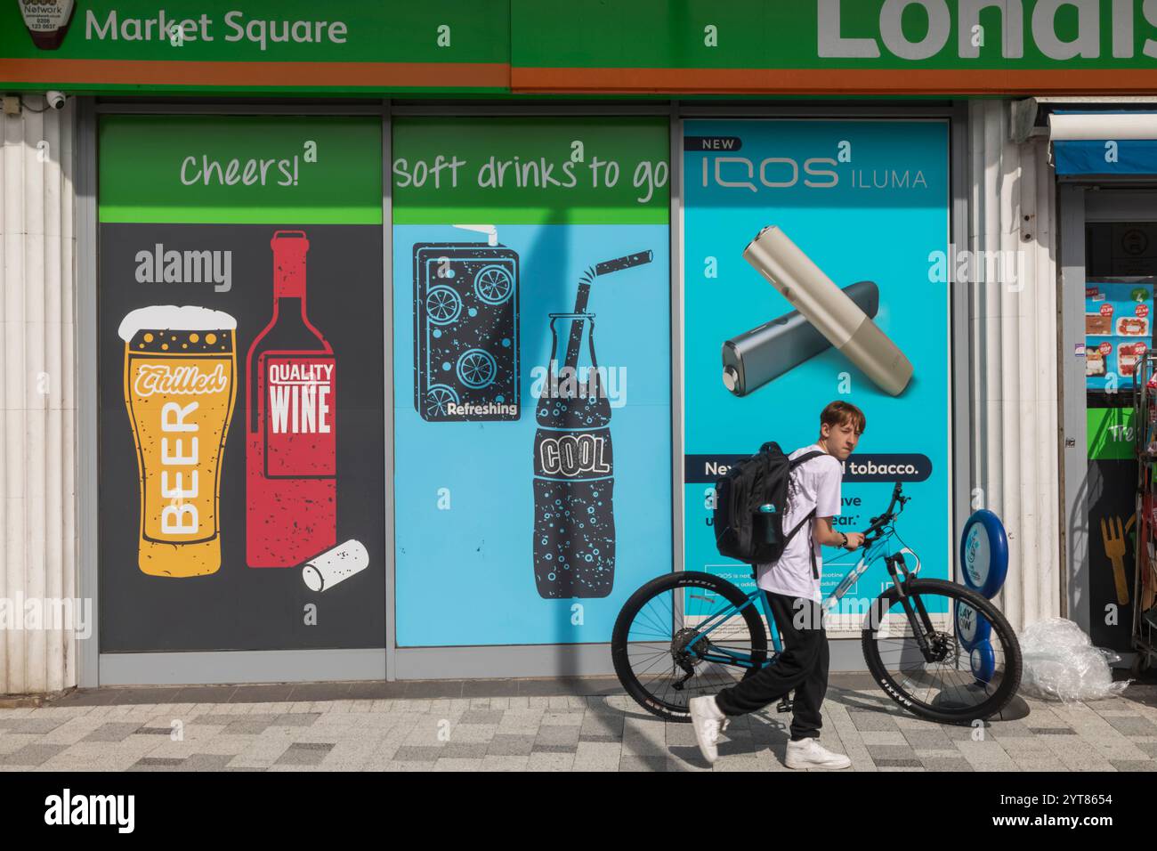 England, Kent, Dover, Straßenszene, junger Mann mit Fahrrad vor der Ladenfront Werbung Alkohol und kohlensäurehaltige alkoholfreie Getränke Stockfoto