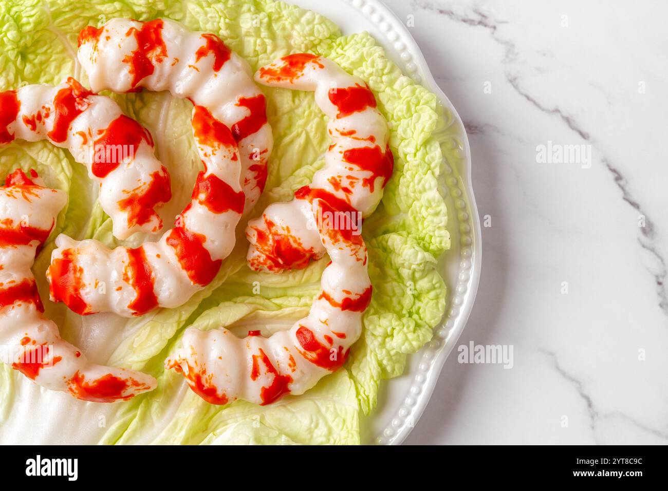 Teller mit roten weißen Surimi-Garnelen auf grünem Salatblatt über Marmorplatte. Garnelen aus Surimi als traditionelle Zutaten der asiatischen Küche. Protein. Stockfoto