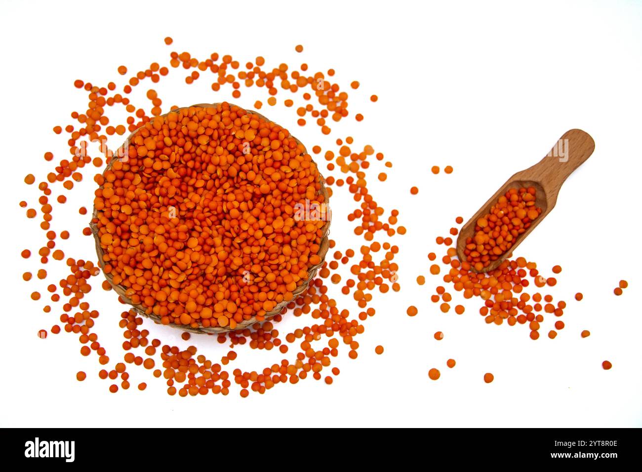 Eine Korbschale gefüllt mit roten Linsen, begleitet von einem Holzlöffel, umgeben von roten Linsenkörnern. Stockfoto