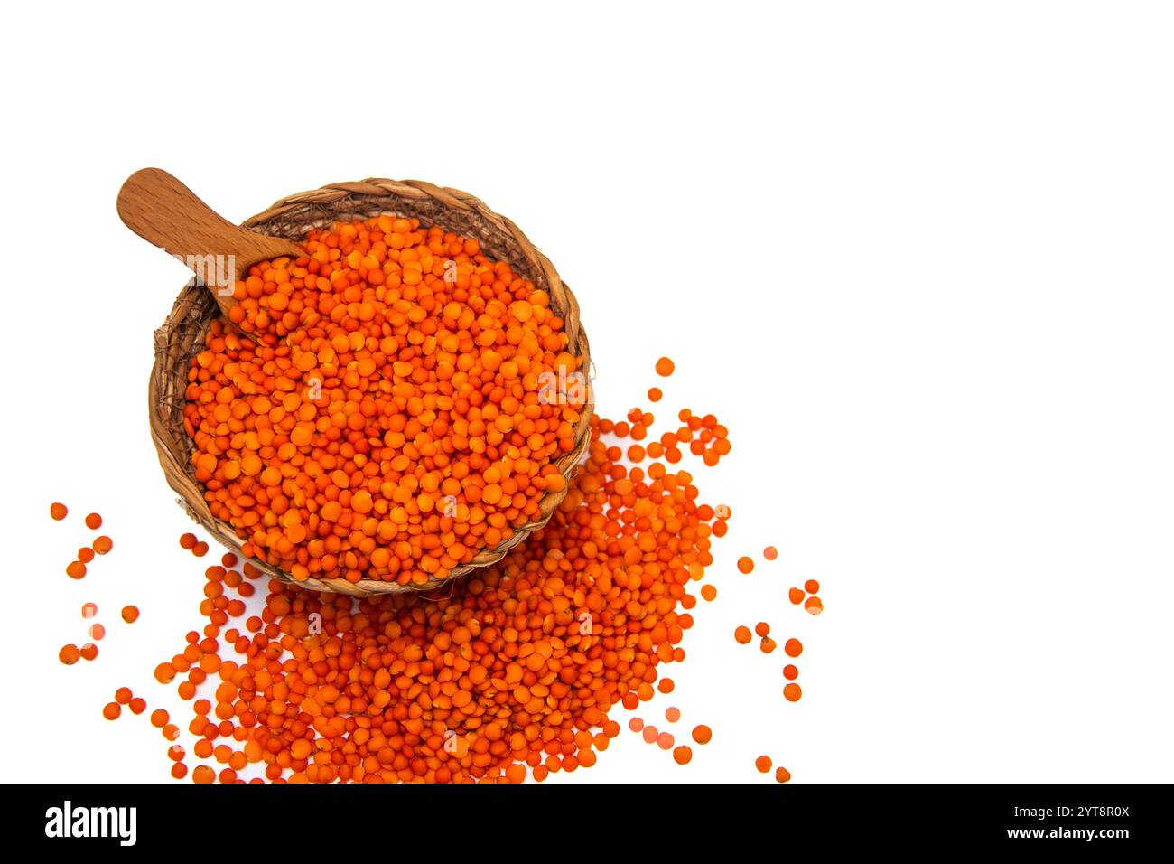 Eine Korbschale gefüllt mit roten Linsen, mit einem Holzlöffel und umgeben von verstreuten roten Linsenkörnern. Stockfoto