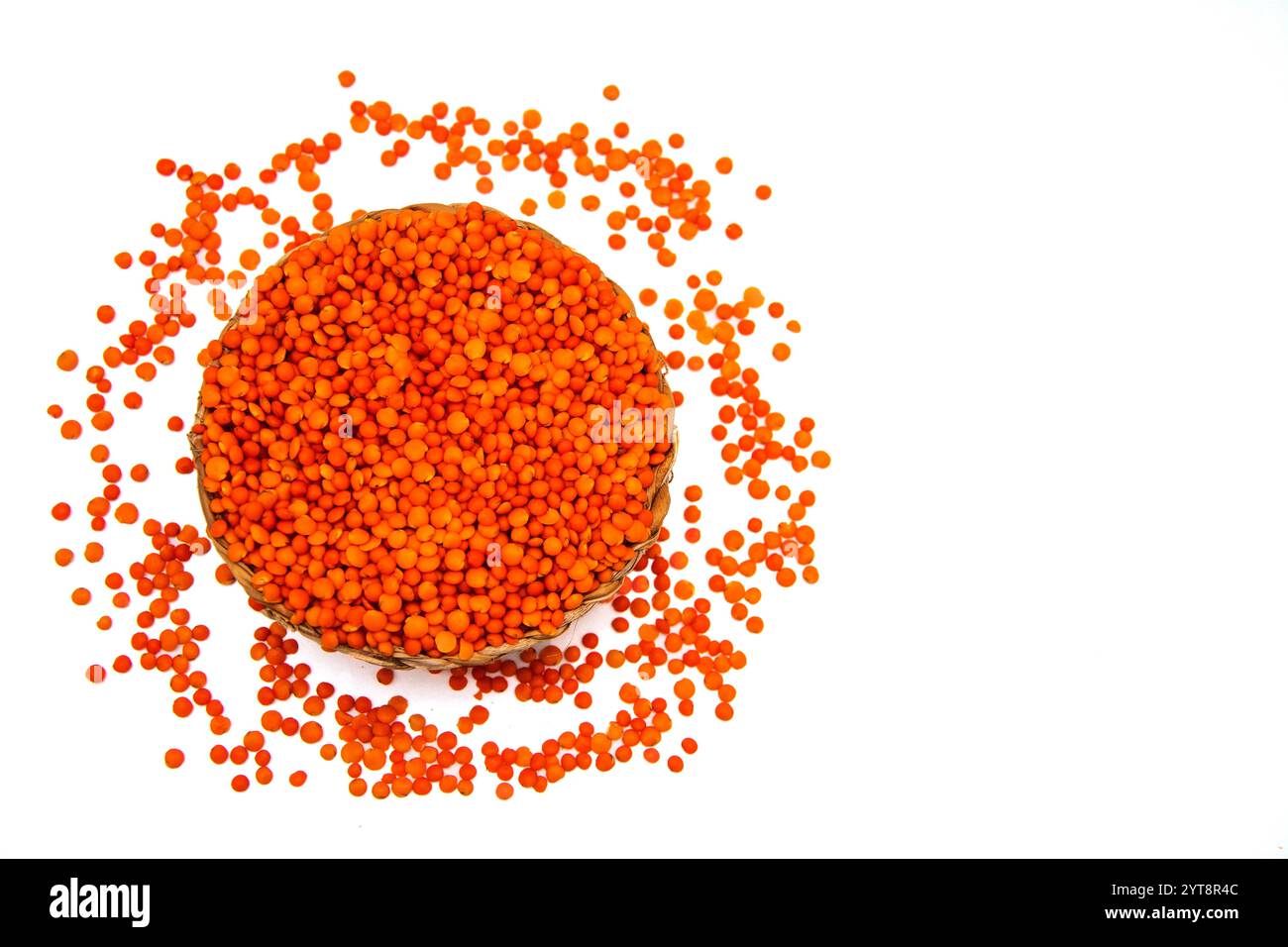 Eine Korbschale gefüllt mit roten Linsen, umgeben von verstreuten roten Linsenkörnern. Stockfoto