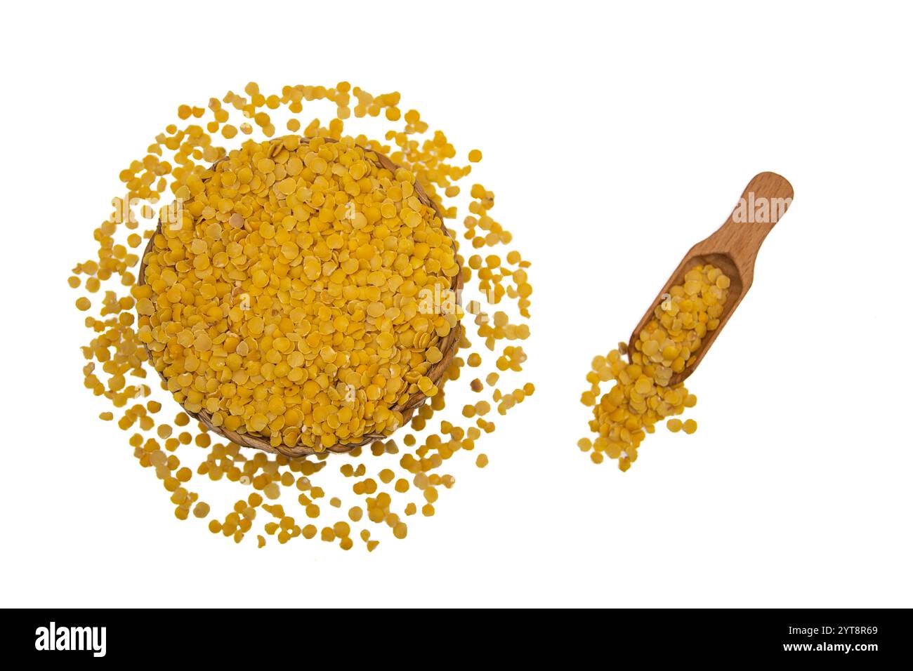 Eine Korbschale gefüllt mit gelben Linsen, begleitet von einem Holzlöffel, umgeben von gelben Linsenkörnern. Stockfoto