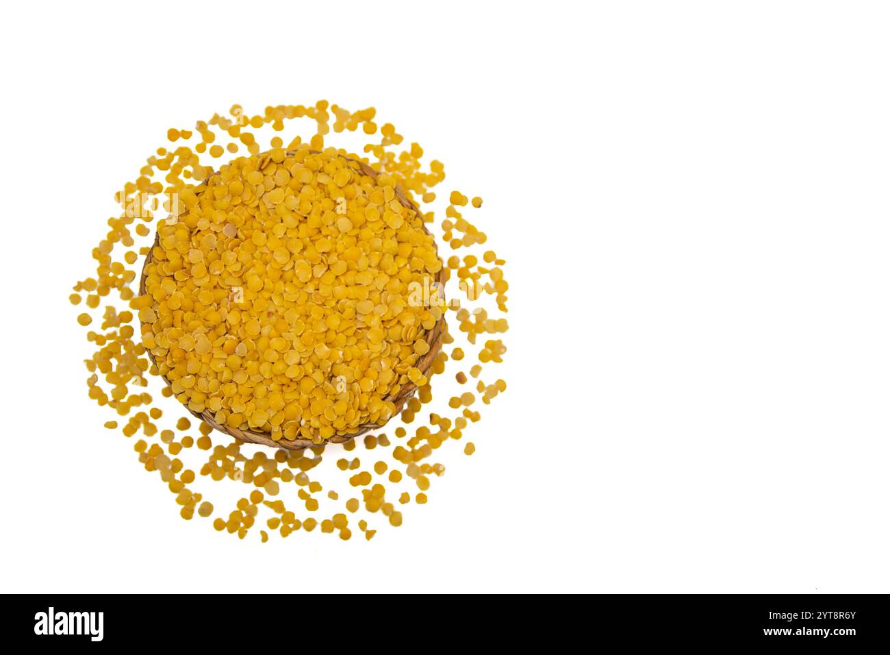 Eine Korbschale gefüllt mit gelben Linsen, umgeben von verstreuten gelben Linsenkörnern. Stockfoto
