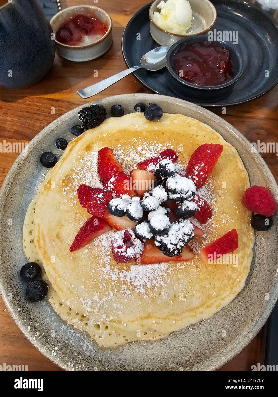 Köstlicher Krepp mit frischen Erdbeeren, Heidelbeeren, Schlagsahne und Puderzucker, serviert mit Marmelade und Vanilleeis auf einem Holztisch. - Smartphone-aufgenommenes Stockfoto