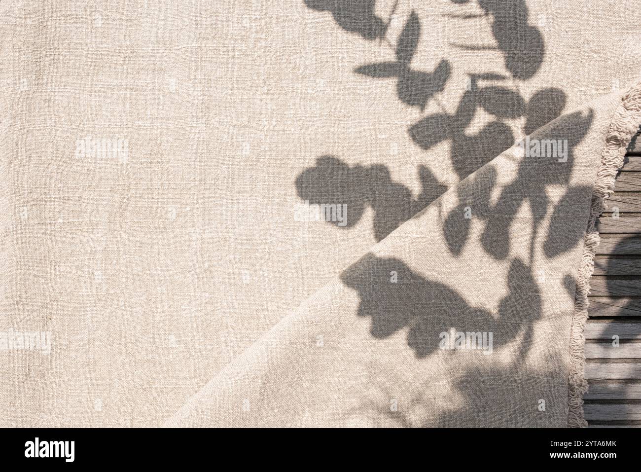 Natürlicher textiler Hintergrund mit Pflanzenschatten im Sonnenlicht. Beigefarbener Leinenstoff auf Holztisch mit Platz für Text. Hintergrund für Hochzeiten im Boho-Stil. Stockfoto