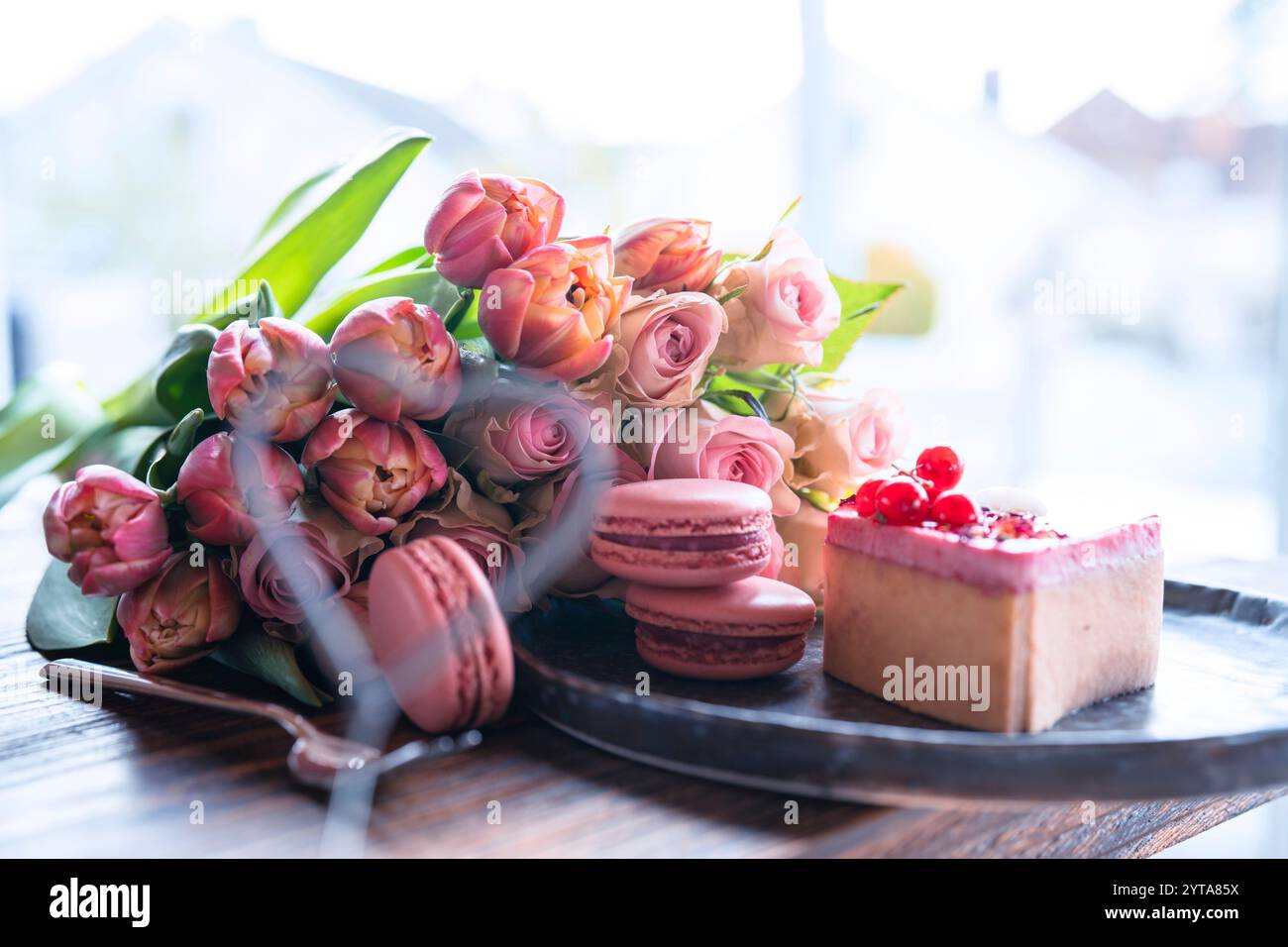 Schöner rosafarbener Blumenstrauß mit süßen Köstlichkeiten. Herzform, süßes Gebäck mit rosa Rosen und Tulpen auf einem Holztisch. Hintergrund für Muttertag und Hochzeiten. Stockfoto