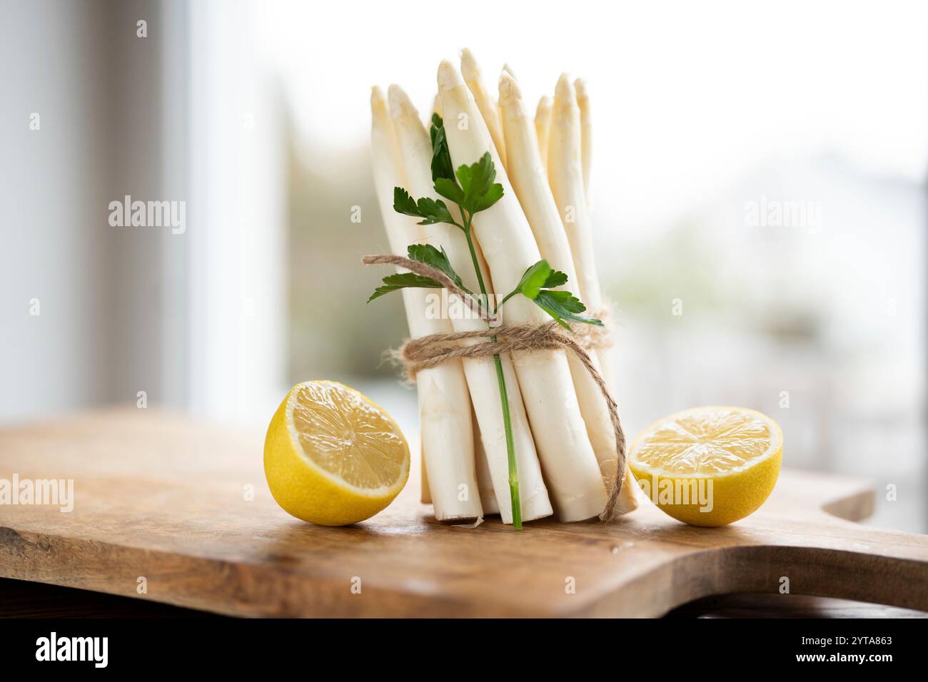 Stehende Haufen frischer weißer Spargel. Saisonales Frühlingsgemüse mit Zitrone und flacher Petersilie auf hölzernem Schneidebrett. Küche für die saisonale Gastronomie. Stockfoto