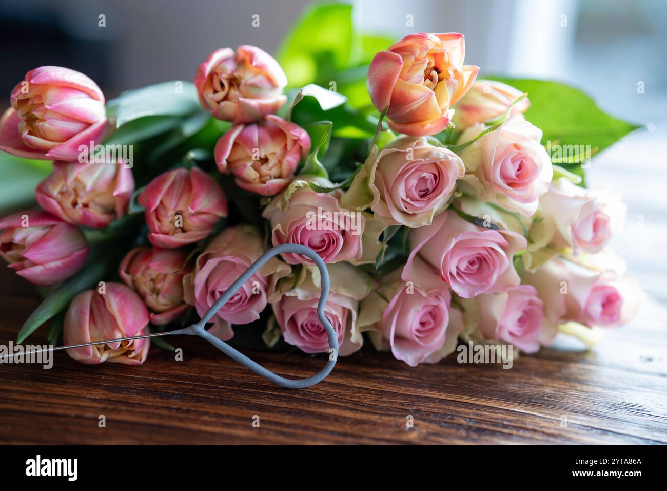 Wunderschöner Blumenstrauß aus rosa Rosen und Tulpen mit Herzform auf dunklem Holz für Muttertagsgrüße. Stockfoto