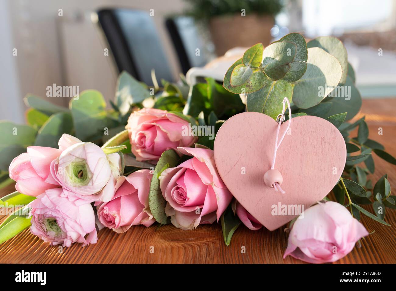 Blumenstrauß aus rosa Rosen mit Ranunkeln und rosa Herzform auf Holztisch für Muttertagsgrüße. Stockfoto