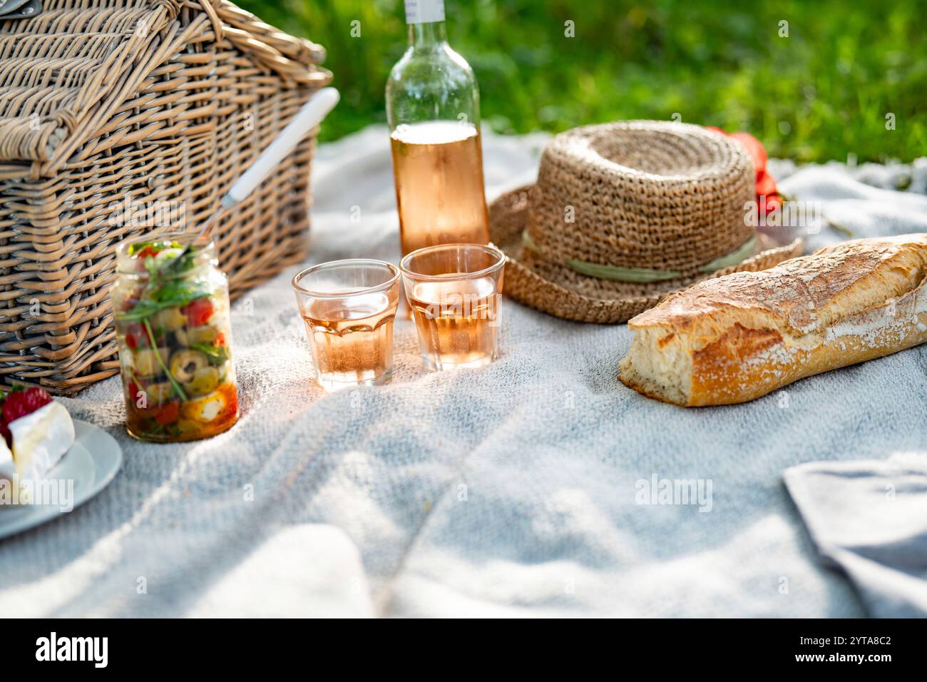 Sommer-Picknick im Park auf Decke mit köstlichem Essen und einer Flasche Rosenwein. Hintergrund mit kurzer Schärfentiefe. Stockfoto