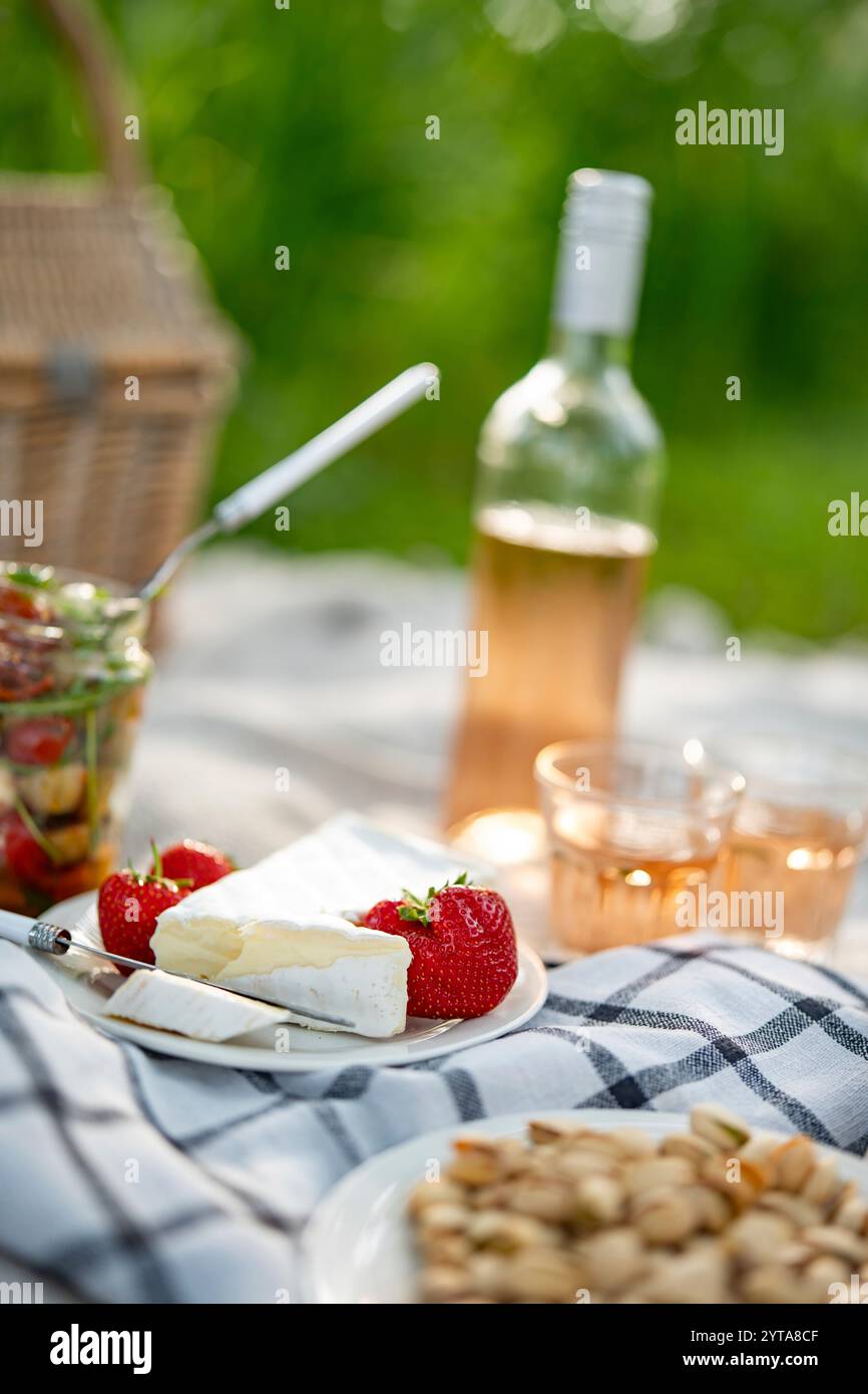 Delikater Camembertkäse und gekühlter Rosenwein bei einem Sommer-Picknick. Vertikale Nahaufnahme mit kurzer Schärfentiefe. Stockfoto