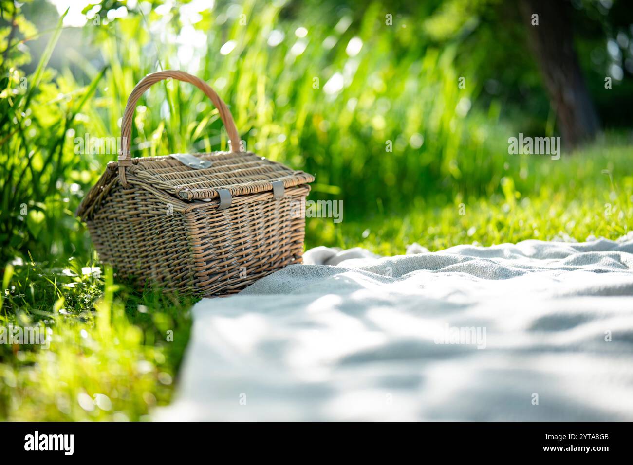 Geschlossener Korb auf Wolldecke. Hintergrund für das Sommer-Picknick im grünen Gras. Nahaufnahme mit kurzer Schärfentiefe. Stockfoto