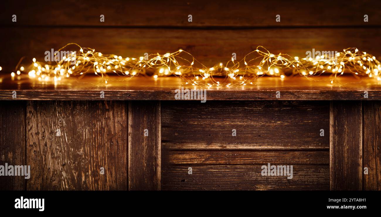 Leere dunkle rustikale Holztheke mit leuchtendem Feenlicht vor der verwundeten Wand. Hintergrund für eine weihnachtsdekoration mit Platz für Text. Stockfoto