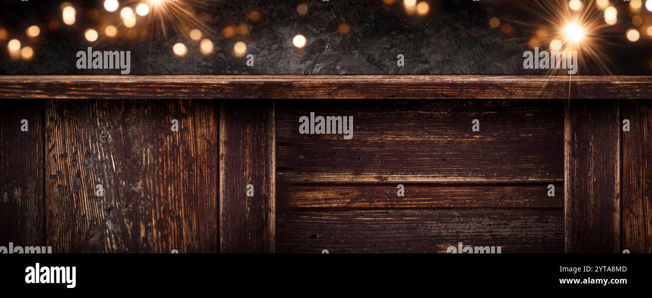 Leere dunkle rustikale Holztheke mit goldenem weihnachtsbokeh vor einer schwarzen Steinmauer. Hintergrund für weihnachtsdekoration mit Platz für Text. Stockfoto