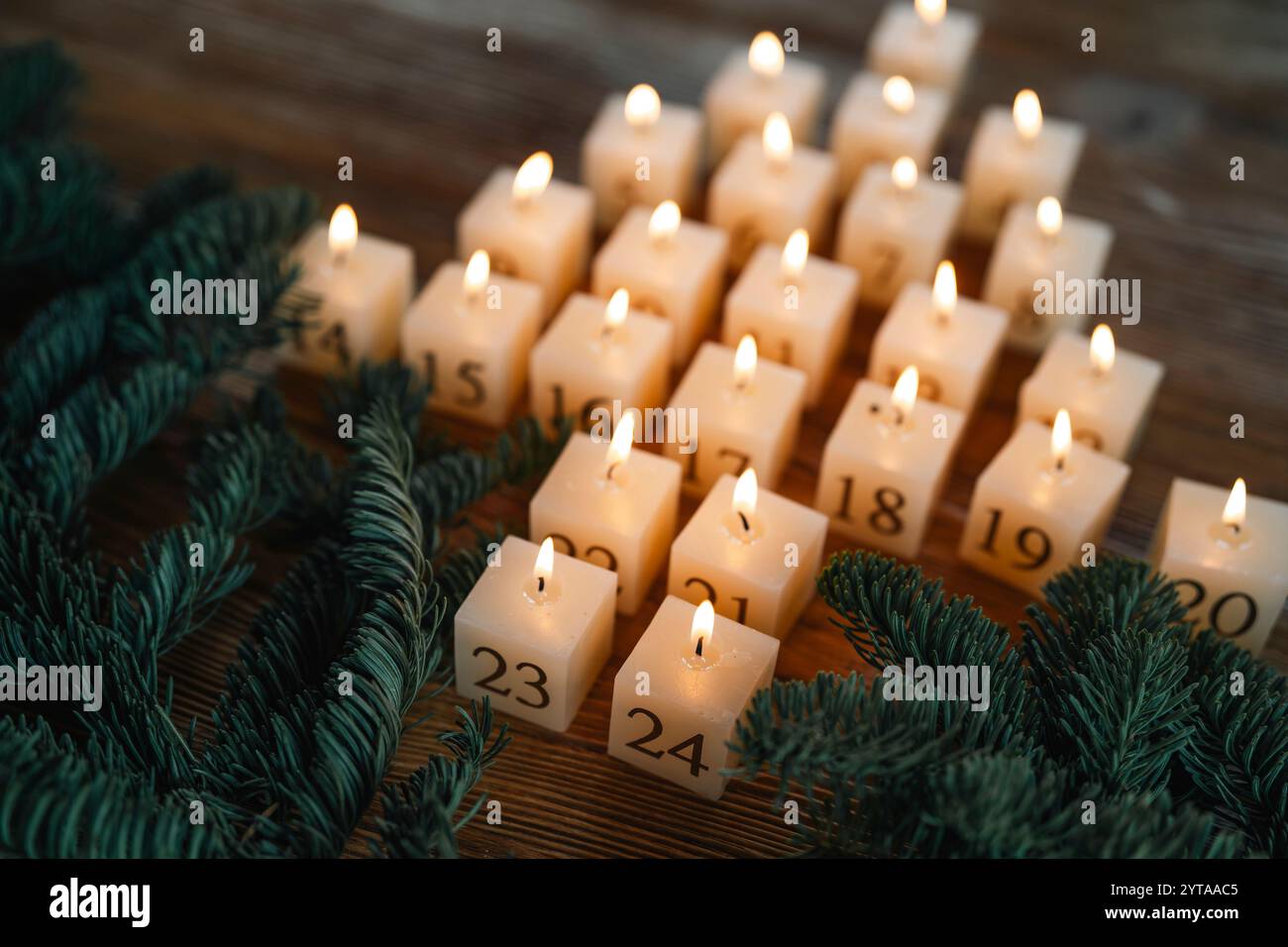 Adventskalender aus 24 brennenden Kerzen. Hausgemachte Kerzen aus natürlichem Bienenwachs. Anordnung in Form eines tannenbaums auf dunklem Holztisch mit Tannenzweigen. Weihnachtlicher Hintergrund mit kurzer Schärfentiefe. Stockfoto