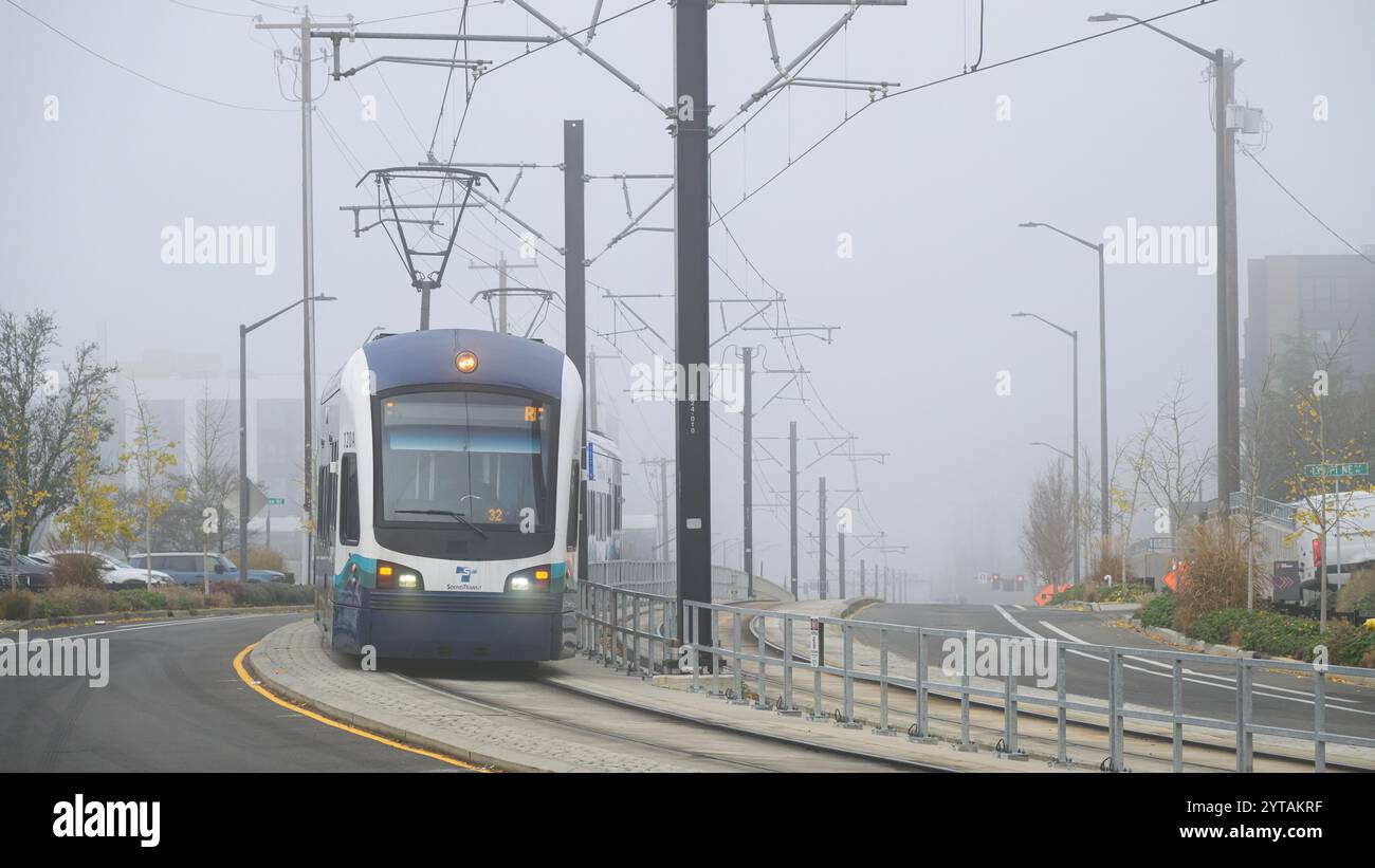 Bellevue, WA, USA - 4. Dezember 2024; Sound Transit Link Stadtbahn im Nebel auf geteilter Straße mit Lichtern und Oberleitungen Stockfoto
