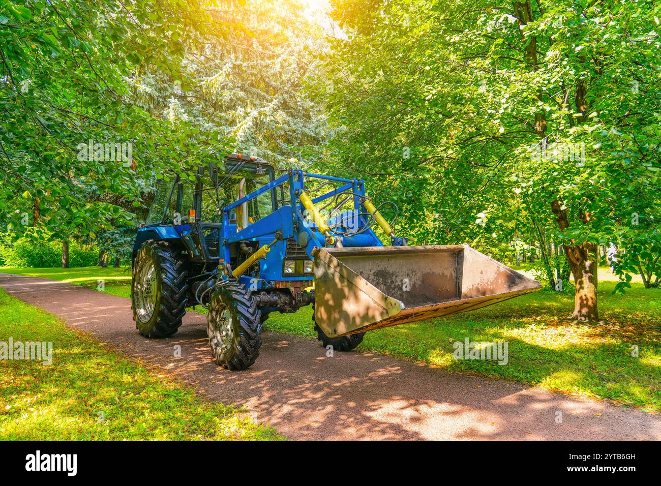 Blauer Traktor mit einer Schaufel im Stadtpark, Wartung des Gebiets. Stockfoto