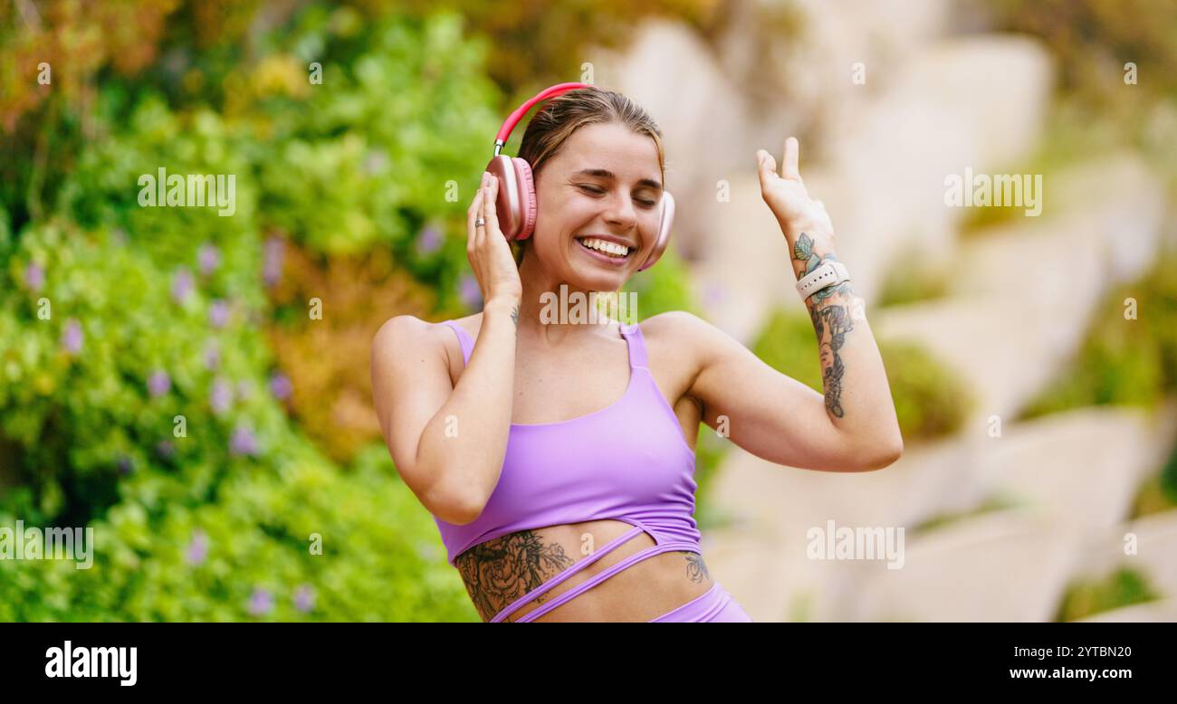 Fröhliche junge Frau, die fröhlich Musik genießt, während sie Zeit im Freien in der Sonne verbringt Stockfoto
