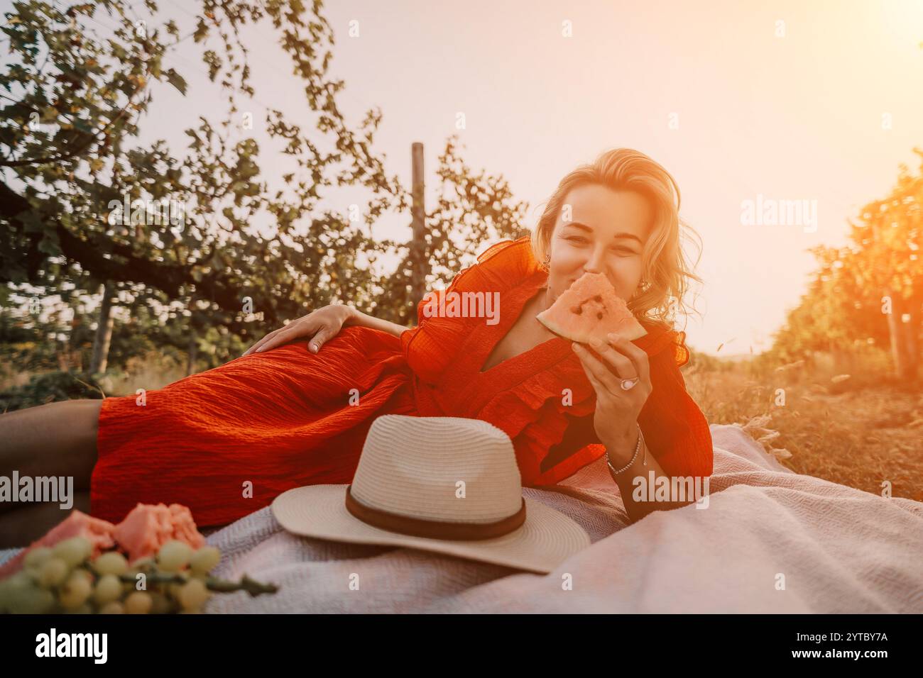 Frau, Picknick, Orchard: Eine Frau genießt ein Picknick in einem sonnigen Obstgarten und legt sich auf eine Decke mit einem Hut neben ihr. Stockfoto