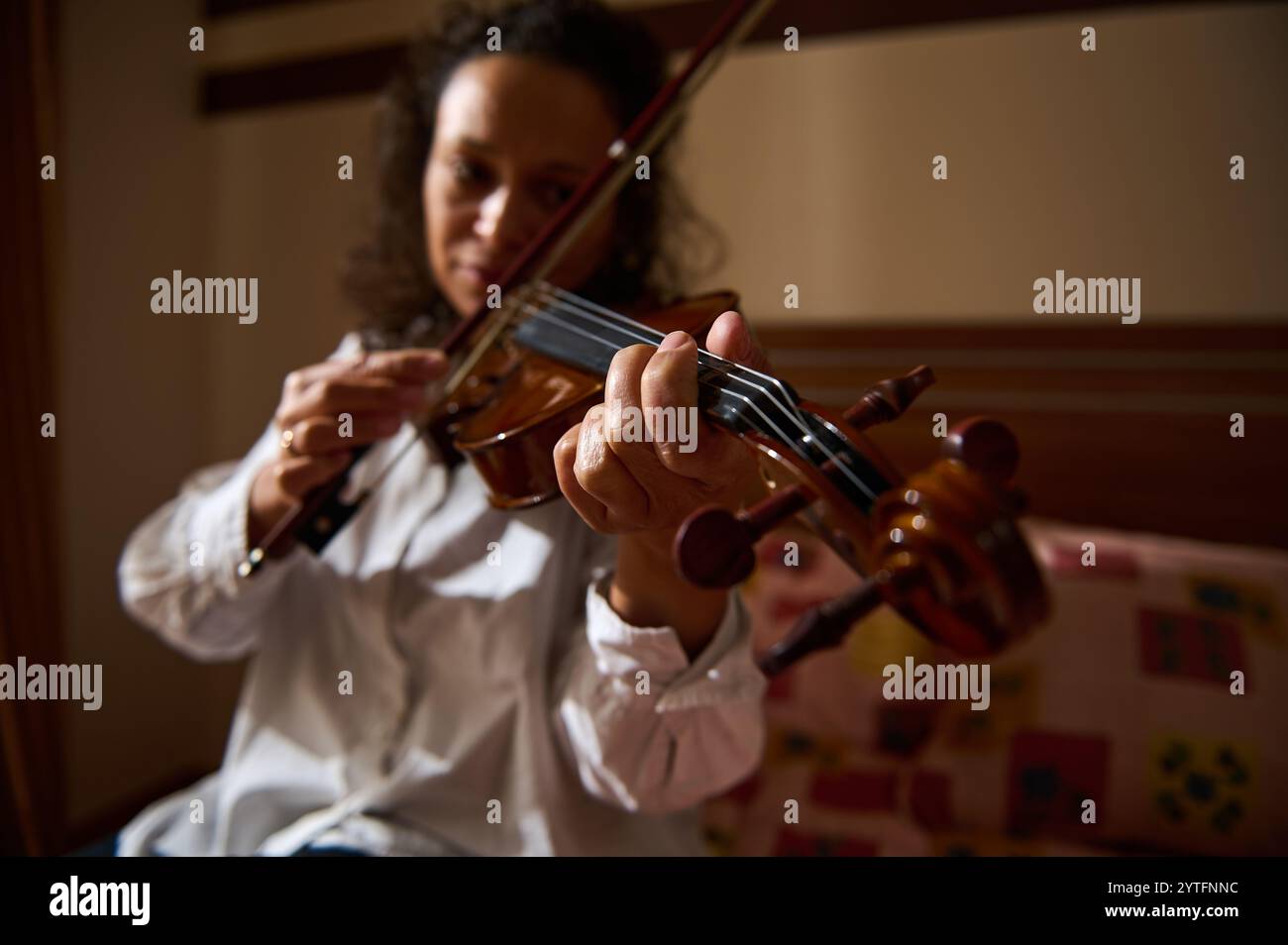 Ein detaillierter Blick auf die Hände, die eine Geige spielen, zeigt die zarte Kunstfertigkeit und den musikalischen Ausdruck in einer intimen Inneneinrichtung. Stockfoto
